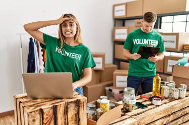 Bağışta gönüllü tişört giyen genç kadın ve adam, elleri kafalarında, şaşırmış ve sinirli bir şekilde ayakta duruyorlar. 