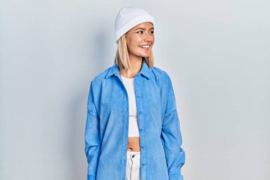 Yün şapka takan güzel sarışın kadın yüzünü yana doğru çevirmiş, doğal bir ifadeyle. Kendinden emin gülen. 