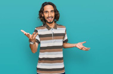 Gündelik kıyafetler giyen genç İspanyol adam güler yüzlü, kolları açık, dostça karşılama, olumlu ve kendinden emin selamlar. 