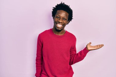 Genç Afrikalı Amerikalı sıradan kıyafetler giymiş neşeli bir şekilde gülümseyen ve avuç içi kameraya bakan biri.. 