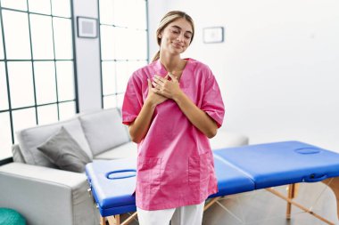 Evde fizyoterapist olarak çalışan genç sarışın kadın elleri göğsünde, gözleri kapalı ve yüzünde minnet dolu bir jest ile gülümsüyor. sağlık kavramı. 