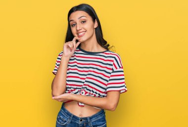 Günlük kıyafetler giyen genç İspanyol kız kameraya kendinden emin bakıyor kollarını kavuşturup gülümseyerek ve çenesini kaldırarak. Olumlu düşünmek. 