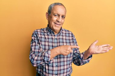 Gri saçlı, sıradan gömlekli yakışıklı bir adam. Kameraya hayret ediyor ve gülümsüyor. Elle ve parmakla işaret ediyor.. 