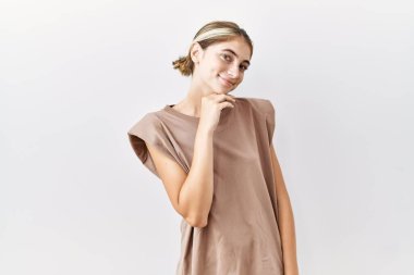 İzole edilmiş arka planda duran genç sarışın kadın kameraya bakarak kollarını kavuşturup gülümseyerek ve çenesini kaldırarak gülümseyerek. Olumlu düşünmek. 