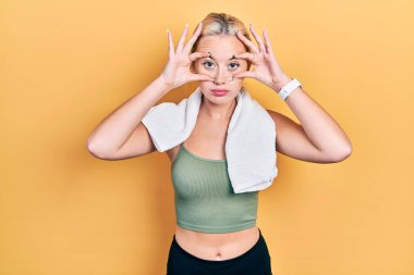 Spor kıyafetleri ve havlu giyen genç sarışın kız parmaklarıyla gözlerini açmaya çalışıyor, uykulu ve yorgun bir şekilde sabah yorgunluğu çekiyor. 