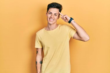 Gündelik sarı tişört giyen genç İspanyol adam tek parmakla başını işaret ediyor, harika bir fikir ya da düşünce, iyi bir hafıza. 