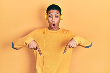 Genç Afro-Amerikalı adam müzik dinliyor kulaklıkla işaret ederek reklam veriyor, şaşırmış yüz ve ağzını açıyor. 