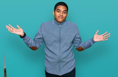 Sıradan bir eşofman üstü giyen, kolları ve elleri havada, kafası karışık, genç, yakışıklı İspanyol bir adam. şüphe kavramı. 