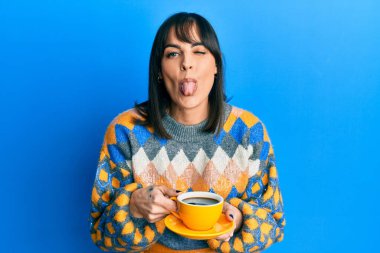 Genç İspanyol kadın bir fincan kahve içiyor. Dilini komik bir ifadeyle dışarı çıkarıyor.. 