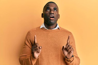 Gündelik giysiler giyen genç Afro-Amerikan adam şaşkın ve şaşırmış bir şekilde yukarı baktı ve parmaklarıyla işaret etti ve kollarını kaldırdı.. 
