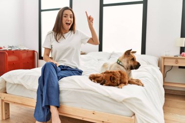 Yatakta oturan esmer bir kadın ve iki köpek başarılı bir fikirle işaret ediyorlar. Heyecanlı ve mutlu. Bir numara.. 