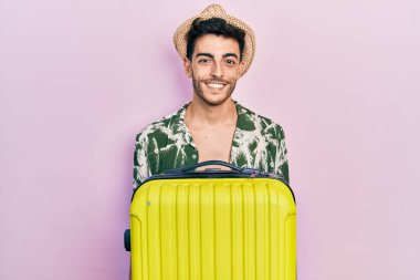 Yaz stili giyinmiş genç İspanyol bir adam ve yüzünde mutlu ve havalı bir gülümsemeyle kamara çantası tutuyor. şanslı kişi. 