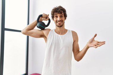 Spor kıyafetleri giyen genç İspanyol adam başarıyı kutlamak için dambıllar kullanıyor. Gülümsüyor ve kazanan el kaldırıyor. 