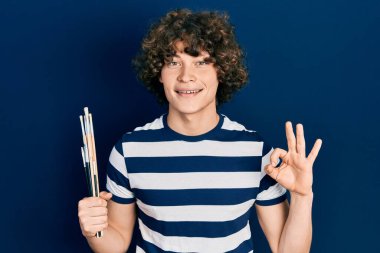 Elinde fırça tutan yakışıklı genç adam parmaklarıyla imza atıyor, gülümsüyor ve mükemmel bir sembol oluşturuyor. 