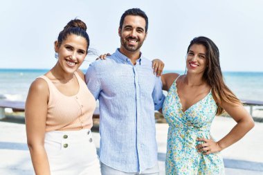 Mutlu gülümseyen ve kumsalda sarılan üç İspanyol genç arkadaş..