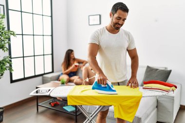 Kadınlar kanepede otururken, erkek gülümseyen mutlu ütü giysileri oturma odasında duruyor..