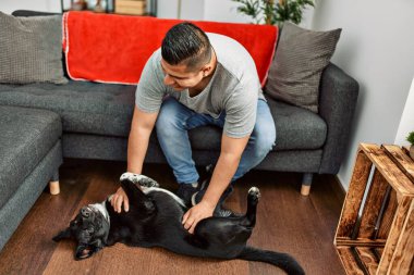 Genç İspanyol gülümseyen adam evde köpekle oynarken mutlu oluyor..