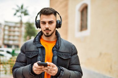 Yakışıklı, sakallı, mutlu ve kendine güvenen, akıllı telefon kullanan, kışlık palto giyen bir İspanyol.