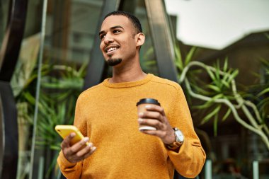 Genç Afrikalı Amerikalı adam akıllı telefon kullanıyor. Şehirde kahve içiyor..