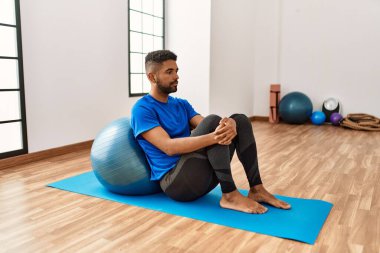 Yakışıklı İspanyol adam egzersiz yapıyor ve yoga minderinde geriniyor, spor salonunda pilates topuyla esneklik gösteriyor.