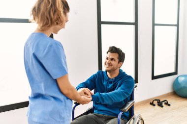 Genç engelli adam ve fizyoterapist klinikte mutlu bir şekilde el sıkışıyor..