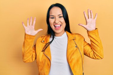 Burnu delinmiş, sarı deri ceketli, güzel İspanyol bir kadın 10 numaralı parmaklarıyla onu gösterirken kendinden emin ve mutlu bir şekilde gülümsüyor.. 