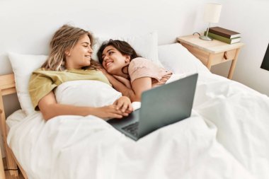 Genç çift yatak odasında dizüstü bilgisayar kullanarak film izliyor.