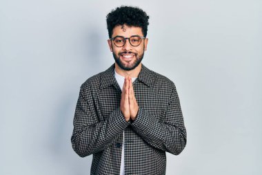 Sakallı, gözlüklü, elleri bağlı dua eden, affedilmek isteyen, kendinden emin gülümseyen genç bir Arap.. 