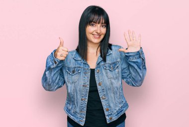 Genç İspanyol kadın gündelik giysiler giyiyor. Altıncı parmaklarını gösterip işaret ederken kendinden emin ve mutlu bir şekilde gülümsüyor.. 