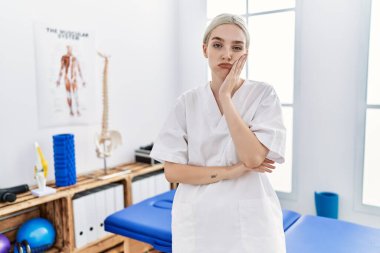 Ağrı kesici kliniğinde çalışan beyaz bir kadın kollarını kavuşturarak depresyondan sıkılmış ve yorgun göründüğünü düşünüyor.. 