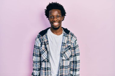 Yüzünde mutlu ve havalı bir gülümseme olan sıradan kıyafetler giyen genç Afro-Amerikan bir adam. şanslı kişi. 