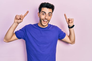 Gündelik tişört giyen genç İspanyol adam şaşırmış, şaşırmış ve parmaklarıyla işaret ederek kollarını kaldırmış.. 