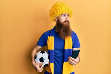 Kızıl saçlı, uzun sakallı futbol holiganları tezahürat yapan akıllı telefon tutan, yan tarafa bakan ve düşünen bir adam.. 