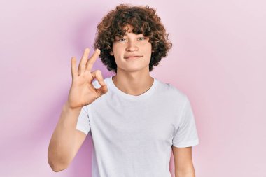 Yakışıklı, beyaz tişört giyen, pozitif gülümseyen, el ve parmaklarıyla 