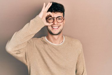 Gündelik kıyafetler ve gözlük takan genç İspanyol adam el hareketleriyle gülümsüyor ve mutlu yüzüyle parmaklarının arasından bakıyor.. 