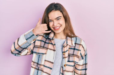 Sıradan kıyafetler giyen, gülümseyen, el ve parmaklarıyla telefon hareketi yapan, telefonda konuşur gibi genç beyaz bir kız. iletişim kavramları. 