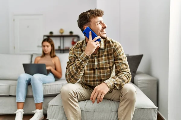 若いヒスパニック系のカップル笑顔幸せな家庭でソファに座ってラップトップとスマートフォンを使用して — ストック写真