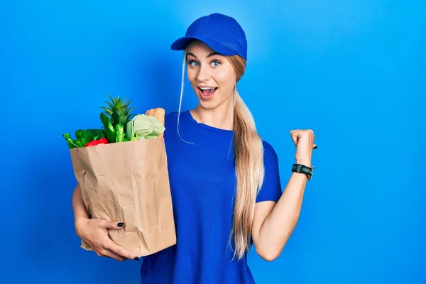 年轻的高加索女人穿着信使制服 带着食品杂货 从超市出来 手背朝后 竖起大拇指 带着自信的笑容 — 图库照片