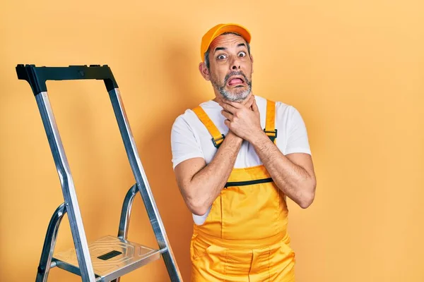 Handsome middle age man with grey hair holding ladder shouting and suffocate because painful strangle. health problem. asphyxiate and suicide concept.
