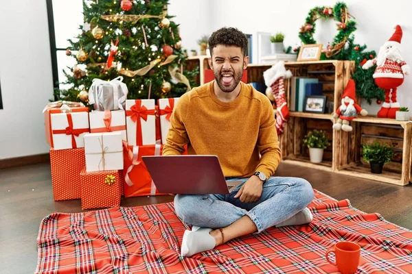 Joven Árabe Usando Portátil Sentado Junto Árbol Navidad Sacando Lengua — Foto de Stock