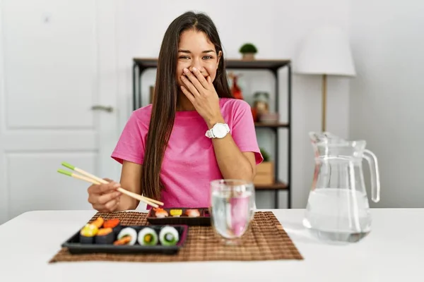 年轻的黑发女人用筷子笑着吃寿司 尴尬地咯咯笑着用手捂住嘴 流言蜚语和丑闻的概念 — 图库照片