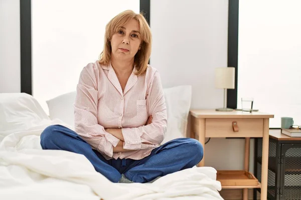 中年の白人女性は 懐疑的で緊張したベッドの上に座っているパジャマを着て 顔に交差した腕で表現を否定しています 否定的な人 — ストック写真