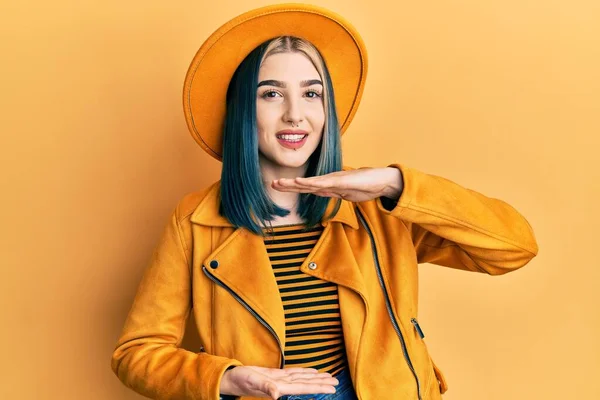 大小のサインを示す手でジェスチャー黄色の帽子と革のジャケットを身に着けている若い現代の女の子は シンボルを測定します カメラを見て笑ってる 概念を測定し — ストック写真