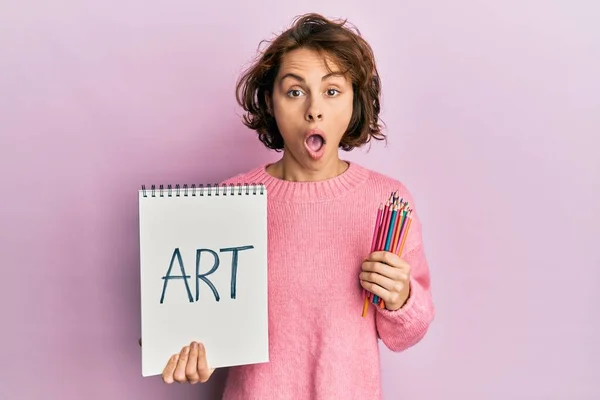 若いですブルネット女性保持アートノートと色鉛筆恐れていると驚きと驚きの表情でショックを受けました 恐怖と興奮した顔 — ストック写真