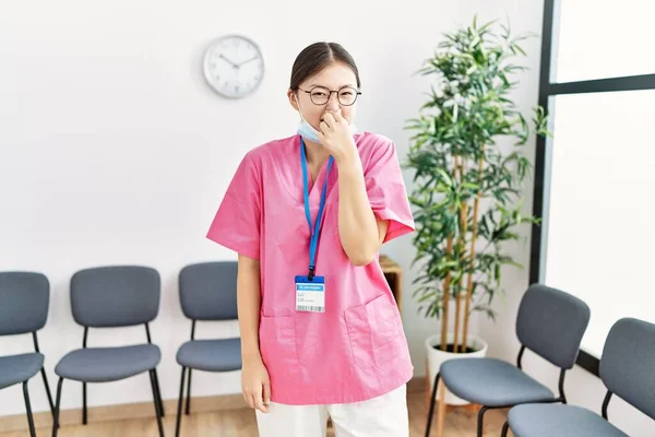 医療待合室の若いアジア人看護師の女性は何か臭いと嫌な 耐え難い匂いを嗅ぎ 鼻の上に指で息を保持します 臭いが悪い — ストック写真