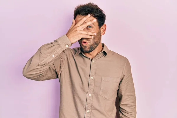 Pohledný Muž Vousy Neformální Košili Vykukující Šoku Zakrývající Obličej Oči — Stock fotografie