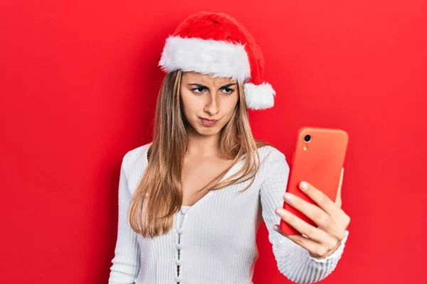 Piękna Latynoska Kobieta Nosząca Świąteczny Kapelusz Pomocą Smartfona Sceptyczna Nerwowa — Zdjęcie stockowe