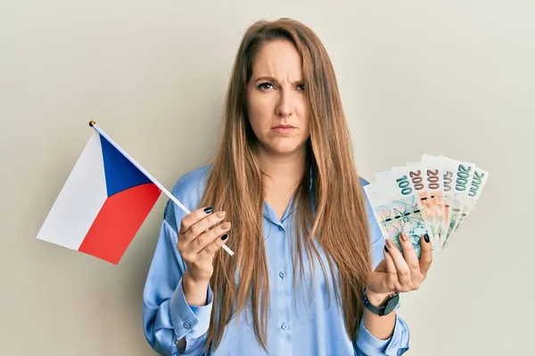 年轻的金发女人拿着切赫共和国国旗和科鲁纳钞票 怀疑而紧张 因为问题皱着眉头 消极的人 — 图库照片