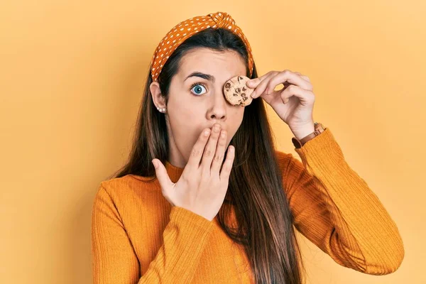 Young Brunette Teenager Holding Cookie Eye Covering Mouth Hand Shocked — Stock Photo, Image