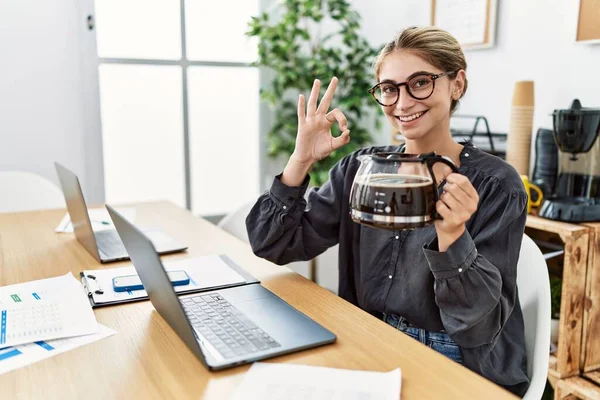 若いですブロンド女性仕事にオフィス保持コーヒーポット行いますOk Signとともに指 笑顔優しいジェスチャー優れたシンボル — ストック写真